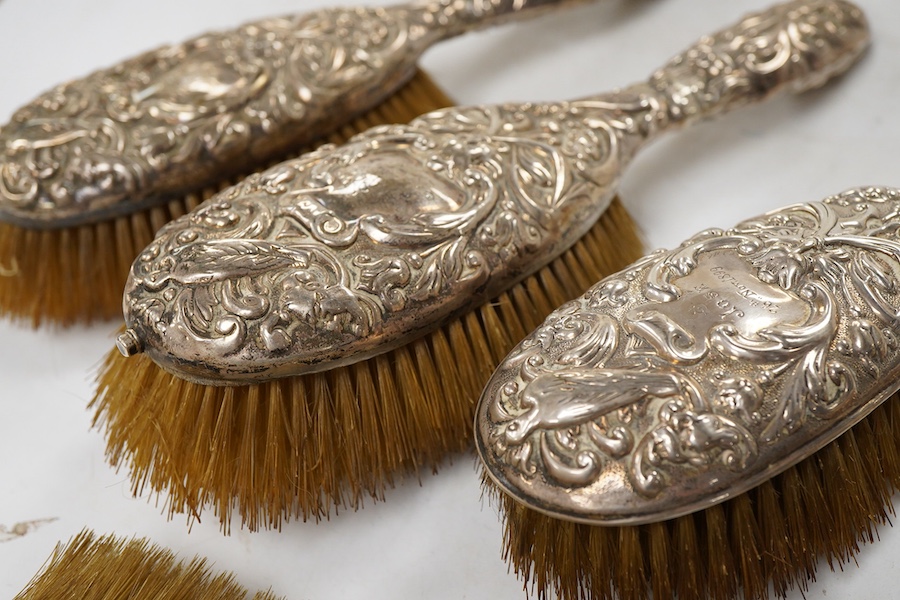 A late Victorian embossed silver four piece dressing table mirror and brush set, by William Comyns, London, 1891/5 and a similar clothes brush.